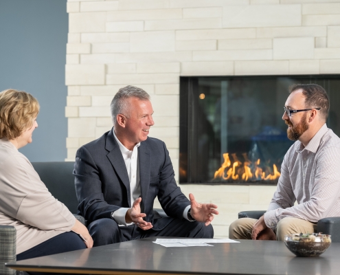 Three Twin Feathers employees sit around table with fireplace in background and discuss marketing strategy.