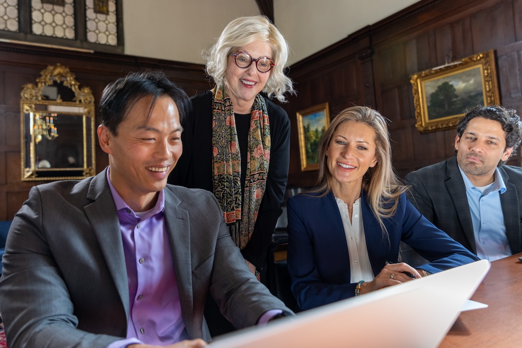 Three professionals in a training session looking at a laptop screen while an instructor looks over their shoulders at the screen.