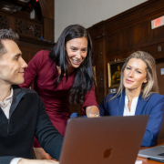 Female training instructor discussing training materials with two attendees who are seated on their laptops.