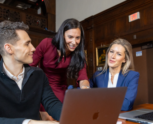 Female training instructor discussing training materials with two attendees who are seated on their laptops.