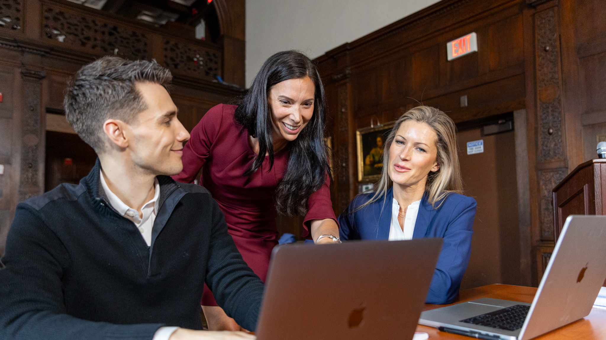 Female training instructor discussing training materials with two attendees who are seated on their laptops.