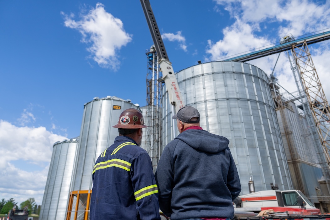 Two Top Bead Welding employees standing outside an industrial area looking up at silos.