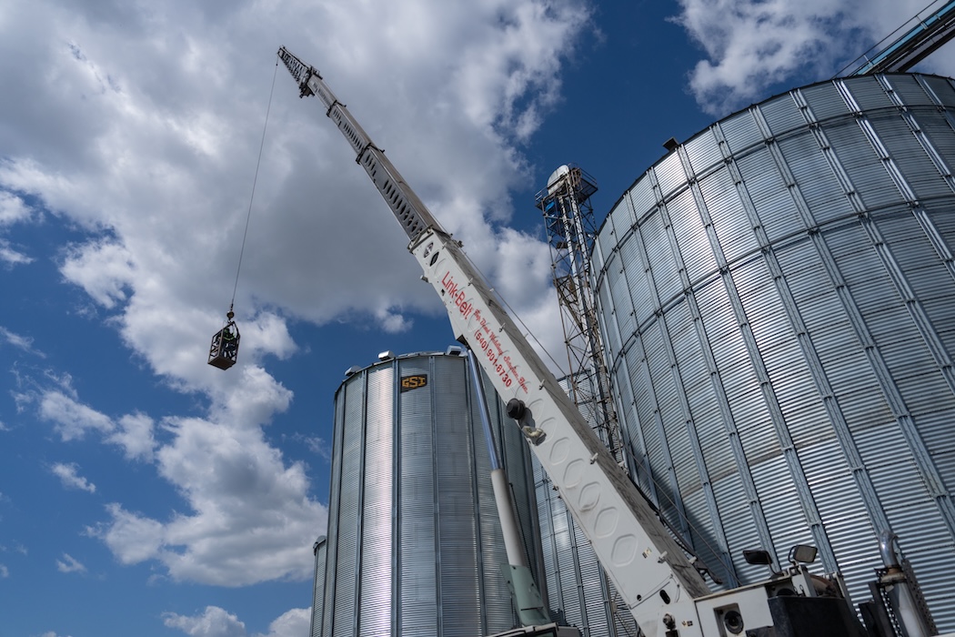 Large crane positioned in front of large industrial silos.