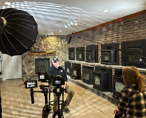 Behind the scenes of a video marketing shoot for an Estland client. Man sits in interview chair with three cameras, lights and boom mic pointed at him.