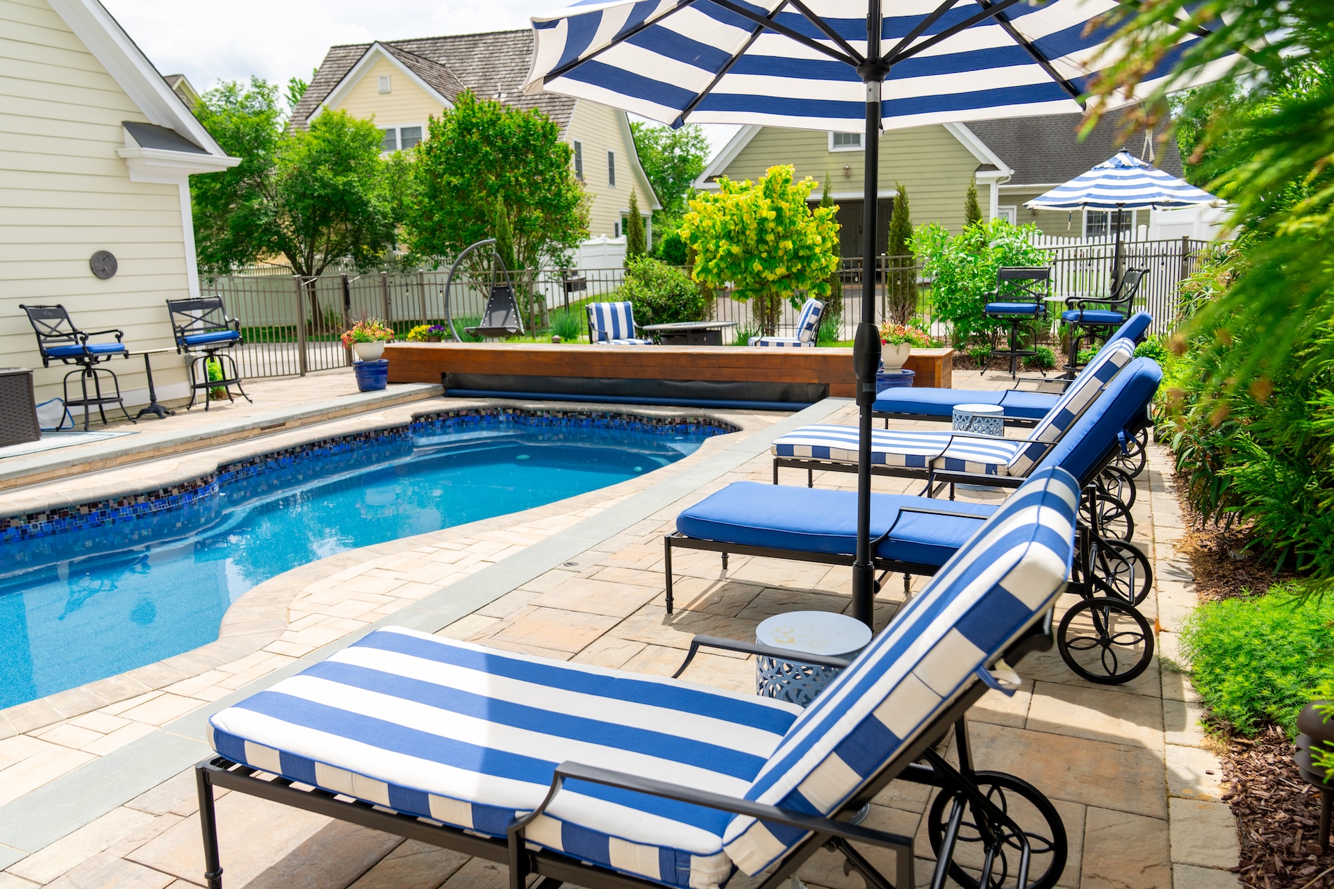 A pool deck with three blue striped lounge chairs and a blue striped umbrella