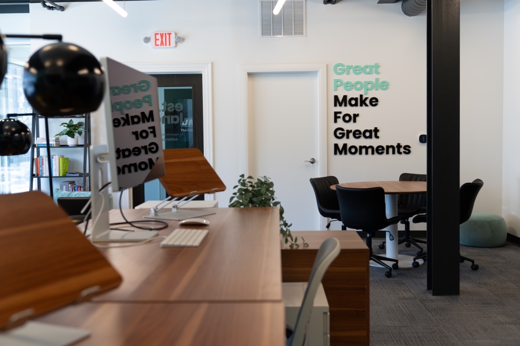 A shot of Estland's new office space, including some desks and monitors, a small conference table and a sign reading "Great People Make for Great Moments" in the background.