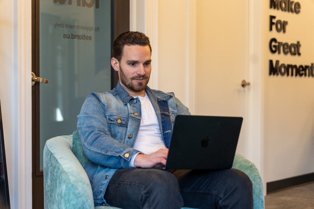 A man in a denim jacket sits with a laptop to write an SEO driven blog.