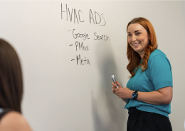 Woman writes on dry erase wall about energy marketing strategies.